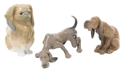 A Lladro porcelain figure of a seated blood hound, together with a hound on its scent, and a porcelain figure of a pekingese. (3)