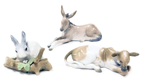 A Lladro porcelain figure of a recumbent calf, another of a donkey, and a figure of a rabbit by a broken tree branch. (3)