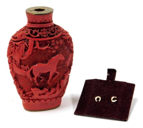 A Chinese red cinnabar lacquer snuff bottle, stopper lacking, carved with horses and trees, 7.5cm high, together with a pair of 9ct gold stud earrings, formed as horseshoes.