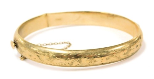 A 9ct gold bangle, with foliate engraving, on a snap clasp, with safety chain as fitted, 10.4g.