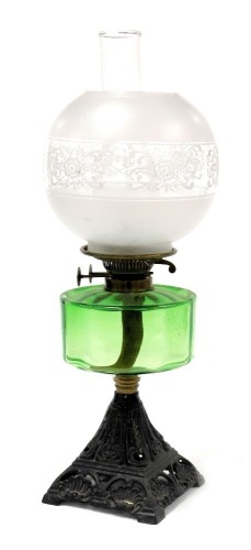 An early 20thC cast iron oil lamp, with a green glass reservoir, glass chimney and etched glass shade, 55cm high.