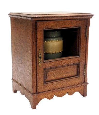 A Victorian oak smoker's cabinet, the glazed and panelled door opening to reveal a pottery tobacco jar and fitted interior, with frieze drawer, raised on stiles united by a shaped apron, 31cm high, 25cm wide, 20cm deep. (AF)