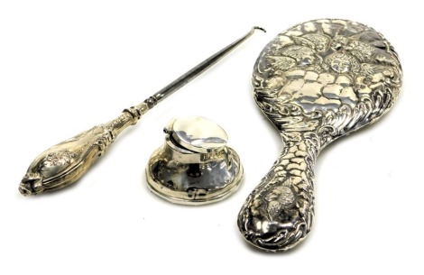 A George V silver handled button hook, with embossed floral decoration, Birmingham 1911, Edward VII silver backed hand mirror, embossed with cherub's heads, and scrolling leaves, Birmingham 1905, and a loaded silver inkwell, hallmarks worn. (3)