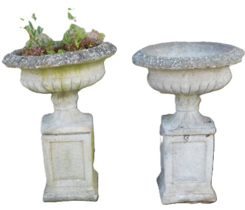 A pair of concrete planters, of semi fluted circular form, raised on an out swept leaf carved foot and square base, raised on block plinths, 75cm high, 55cm diameter.