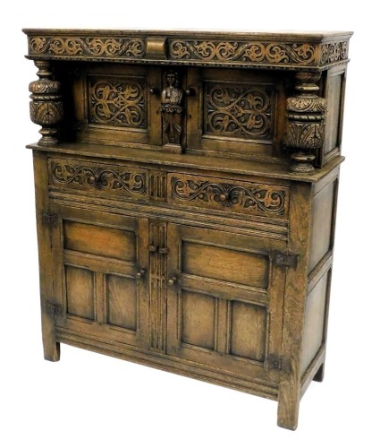 An Elizabethan style oak court cupboard, with a scrolling floral carved frieze, above a pair of panelled doors, flanking a caryatid, on carved cup and cover supports, above two frieze drawers over a pair of panelled doors, raised on stiles, 145cm high, 12