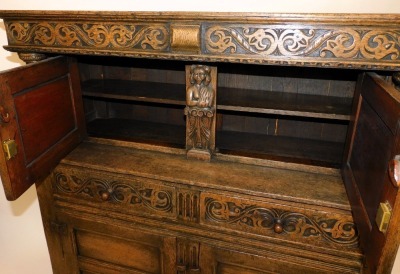 An Elizabethan style oak court cupboard, with a scrolling floral carved frieze, above a pair of panelled doors, flanking a caryatid, on carved cup and cover supports, above two frieze drawers over a pair of panelled doors, raised on stiles, 145cm high, 12 - 3