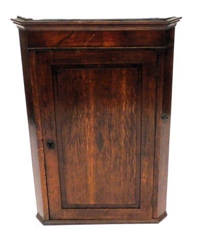 A Georgian oak and mahogany wall hanging corner cupboard, with an outswept pediment over a single panelled door opening to reveal three shelves, 97cm high, 66cm wide, 36cm wide.