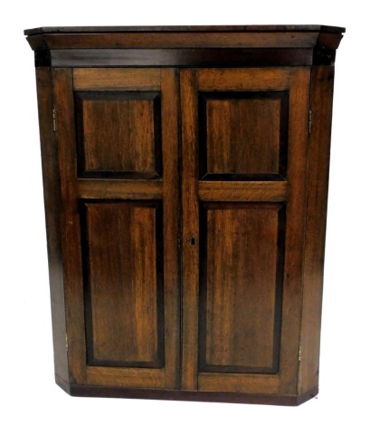 A Georgian oak and rosewood banded wall hanging corner cupboard, with an outswept pediment over a pair of door enclosing two shelves, 99cm high, 79.5cm wide, 41cm deep.