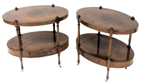 A pair of Georgian reproduction mahogany side tables, of oval, two tier form, with a single frieze drawer, raised on turned supports, brass capped on castors, 60cm high, 65cm wide, 43.5cm deep.