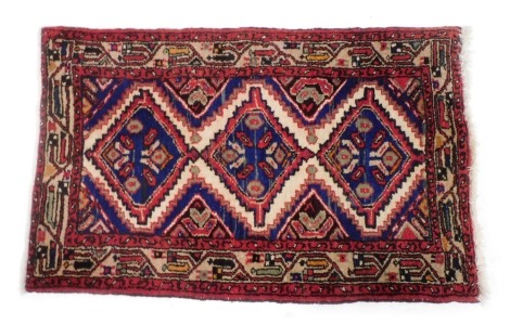 A Hamadan type red ground rug, with three central geometric medallions, within a repeating floral and foliate border, 117cm x 74cm.