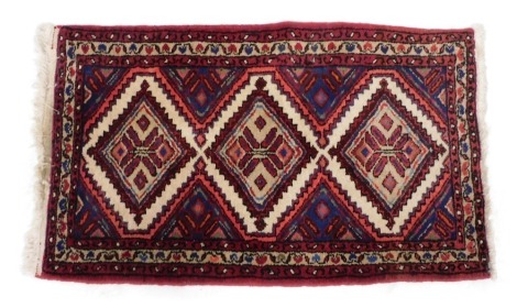 A Hamadan type red ground rug, with three central geometric medallions, within a repeating floral and foliate border, 127cm x 73cm.