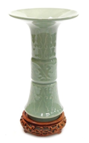 A Chinese Longquan celadon porcelain gu-shaped vase, with incised scrolling decoration between bands of lappets, 25cm high, on a wooden stand.