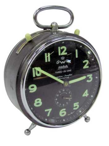 A 1960s Wehrle three in one steel cased alarm clock, the black circular dial bearing glow in the dark Arabic numerals, subsidiary dial for hourly alarm setting, with ring handle, 13cm high.(AF)