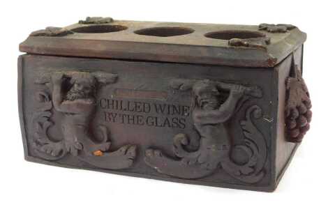 A painted wooden wine bottle stand, for three bottles, modelled in the form of a casket, carved with figures, leaves, vine motifs, etc, 47cm wide.