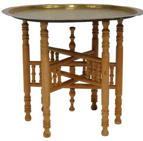 An Egyptian brass tray top occasional table, raised on a folding wooden base, 53cm high, 64cm diameter.