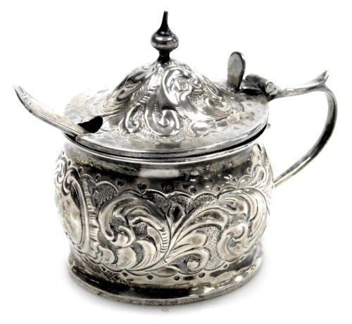 A Victorian silver mustard, with hammered foliate scroll decoration, with blue glass liner, and later caddy spoon, John Millward Banks, Birmingham 1892, 1.43oz.