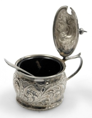 A Victorian silver mustard, with hammered foliate scroll decoration, with blue glass liner, and later caddy spoon, John Millward Banks, Birmingham 1892, 1.43oz. - 2