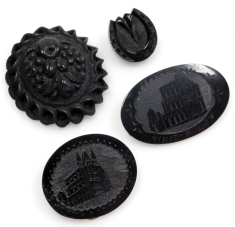 Four jet brooches, comprising a Victorian carved jet brooch, with floral basket, 6cm diameter, a Whitby Abbey oval brooch, 6cm wide, a View of Whitby Abbey brooch, 4.5cm wide, and a horseshoe brooch, 2.5cm wide, each on brass pin back, one lacking back, 5