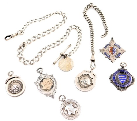 Two various silver curb link watch chains, and various crested fobs, comprising a partially curb link chain with clip, 17cm long, and a further clip and T bar, 37cm long, two silver Cycling Award badges, a Kingston and District Football League blue enamel