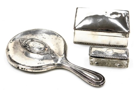 An Edward VII cut glass and silver lidded pin box, Birmingham 1906, George V silver backed hand mirror, Birmingham 1911, and a silver plated cigarette casket, 13cm wide. (3)