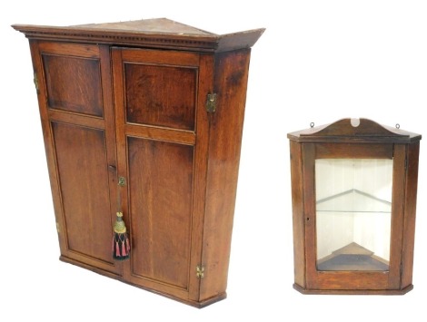 A Georgian oak wall hanging corner cupboard, with a pair of panelled doors, 100cm high, 84cm wide, 55cm, together with a further oak wall hanging corner cupboard, with a glazed door enclosing a glass shelf, 69cm high, 52cm wide, 30cm deep.