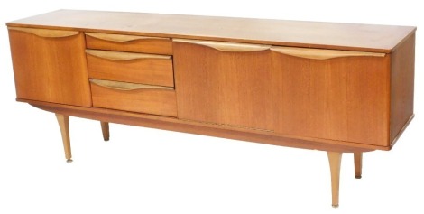 A Stonehill teak sideboard, with three graduated drawers, flanked to the left by a cupboard, to the right with a drop down drinks cabinet, and a further cupboard, raised on tapering square legs, 75cm high, 197cm wide, 45.5cm deep.