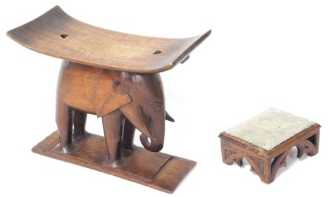 An African Ashanti hardwood stool, with a curved seat, raised on an elephant, above a rectangular base, 58cm wide, together with a Victorian Gothic oak footstool, 33cm wide. (2)