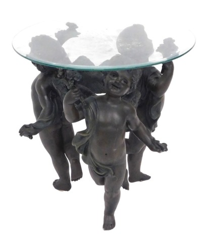 A bronzed plaster and glass topped occasional table, raised on three cherub supports, 60cm high, 60cm wide.