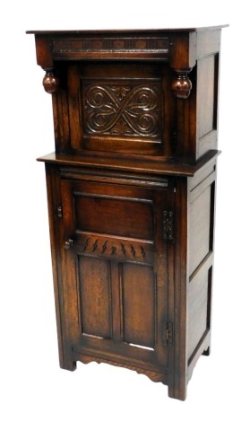 An oak court or press cupboard, with a rectangular top, above a carved panelled door enclosing a single shelf, above a cupboard door, enclosing a further shelf, on stiles, 136cm high, 61cm wide, 40cm deep.