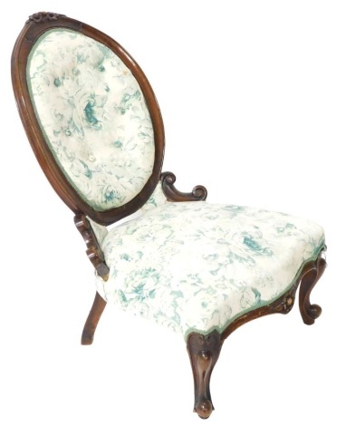 A Victorian mahogany spoon back nursing chair, with floral carved crest rail, button back and overstuffed seat in blue rose fabric, raised on cabriole legs, 55cm wide.