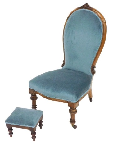 A Victorian mahogany spoon back nursing chair, upholstered in light blue draylon, raised on turned legs, brass capped on castors, 52cm wide, together with a mahogany footstool, upholstered in the same fabric, 28cm wide. (2)