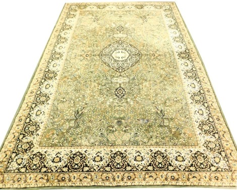 A Kashan green and cream ground rug, the central field decorated with a medallion, flowers and birds, within repeating floral borders, 406cm x 272cm.