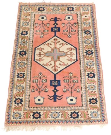 A Caucasian pink ground rug, the central field decorated with a medallion, and urns of flowers, within repeating geometric and floral borders, 194cm x 130cm.