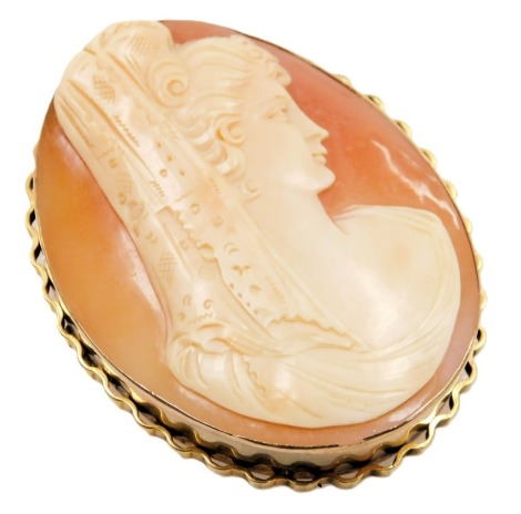 A shell cameo brooch, bust portrait of a lady in a mantilla, set in yellow metal, with safety chain as fitted.