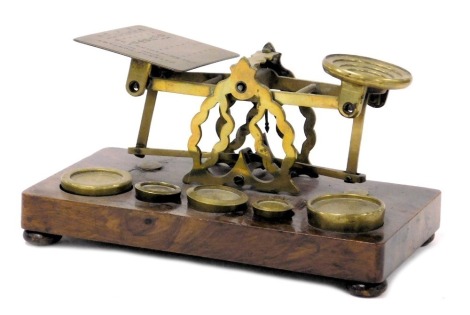 A set of Victorian brass postal scales, with weights, raised on a walnut base, 21.5cm wide.