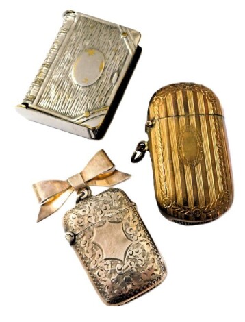 A Victorian silver vesta case, with foliate engraving, vacant shield reserve, Birmingham 1898, on a silver bow suspension, stamped sterling, 0.63oz, together with a silver plated vesta case, modelled as a book, and a brass vesta case. (3)