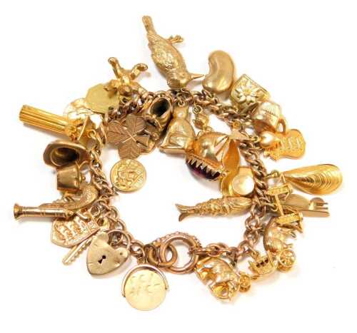 A 9ct gold gate bracelet, with a curb link bracelet and safety chain, heart shaped padlock and various charms to include a cat, oyster, London Bridge, Jersey shield, seal fobs and others, three loose, mainly stamped 9ct, 14cm long, 54g all in.