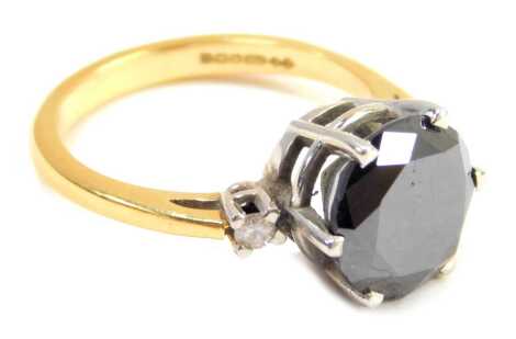 An 18ct gold dress ring, with a central black metallic round brilliant cut stone, in a six claw raised basket setting, with tiny diamonds to each side, in white gold on a yellow metal band, ring size M½, 5.3g all in.