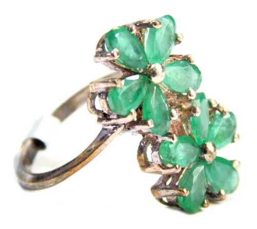 A Coloured Rocks dress ring, formed as two five point floral clusters, each set with emeralds, on white metal stamped 925, ring size K. 3.3g all in, boxed.