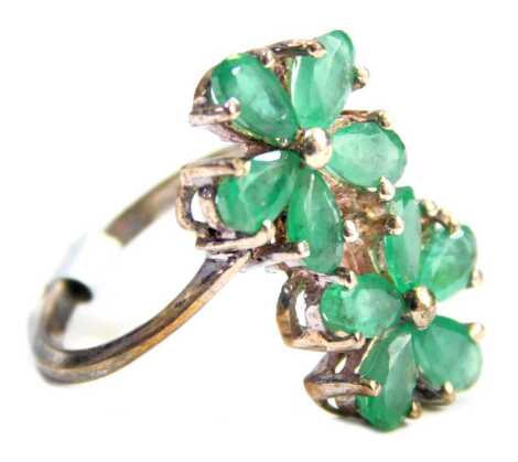 A Coloured Rocks dress ring, formed as two five point floral clusters, each set with emeralds, on white metal stamped 925, ring size K. 3.3g all in, boxed.