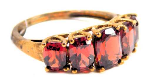 A five stone garnet dress ring, set with five graduated oval cut garnets, in a raised basket claw setting, on a yellow metal band, stamped 9kt, ring size N½, 2.6g all in, boxed.