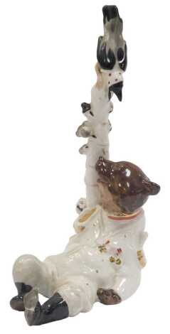 A Russian porcelain figure, modelled as a seated bear in military uniform leaning against tree with bird to top, 22cm high.