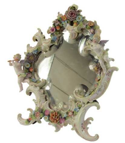 A late 19thC German porcelain strut mirror, decorated with putti, flowers, etc., in a rococo style scrollwork frame, with bevelled glass mirror, 42cm x 35cm.