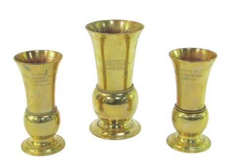 Three brass ecclesiastical related vases, each with a flared neck, bulbous body, on a stepped circular foot, a pair inscribed 'In Memory of William Henry Hemsell 6th March 1959, and Secretary for 23 Years', 20cm high, the other larger example bearing insc