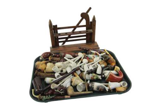 Smoking related items, to include an oak pipe stand, 27cm high, various clay pipes, wooden pipe, porcelain pipes with transfer printed decoration, etc. (1 tray)