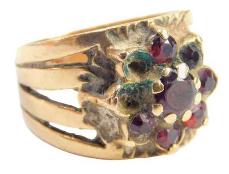 A garnet floral cluster dress ring, the central cluster claw set, with striped border, on four splayed shoulders, yellow metal, unmarked, size N, 6.4g all in. (AF)