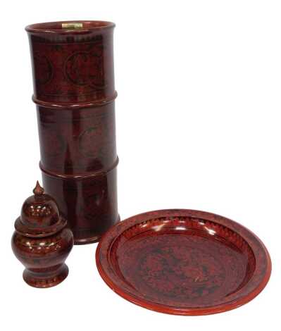 A group of Eastern red lacquered wares, comprising cylindrical umbrella stand, 62cm high, charger, 43cm diameter, and jar and cover, 28cm high, each decorated with floral motifs, birds, etc.