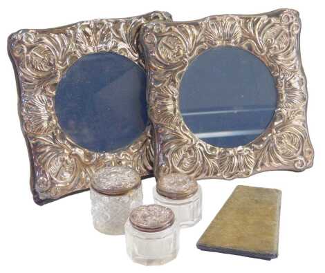 A pair of Elizabeth II silver photograph frames, with hammered shell and scroll detail, Sheffield 1992, with blue velvet back, lacking support, 14cm x 14cm, and three silver topped and cut glass dressing table jars.