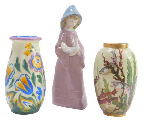 A group of ceramics, comprising a Nao figure of a girl holding a dove, 25cm high, Crown Ducal floral vase, 19cm high, and a Crown Staffordshire fish painted vase, 19cm high. (3)