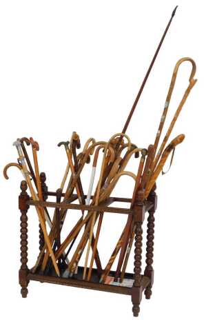 A 20thC oak stick stand, with three sections for sticks, with shaped end supports, on turned cylindrical feet, 75cm high, 78cm wide, 29cm deep, together with a collection of wooden walking sticks, and a bow.